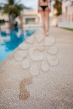 footprints on the wooden surface with blue swimming pool on the background. Summer concept
