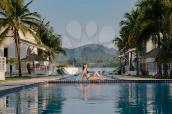 summer holidays in luxury hotel, woman relaxing near beautiful swimming pool. Beauty and body care. Back view, without face