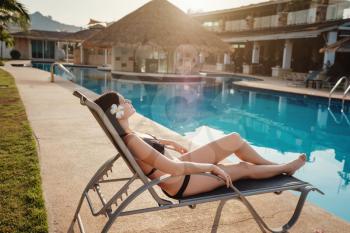 Happy young woman in swimsuit laying on chaise-longue poolside. The concept of a summer holiday.