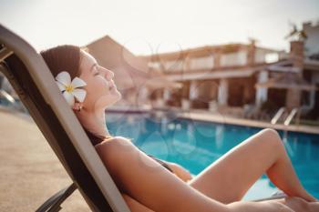 Shot of a young woman relaxing by the luxury pool. Summer vacation. Happy woman enjoying sunny summer day at the poolside. Summer holiday idyllic.