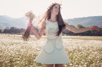 Beautiful young girl smiling over chamomile field. Carefree happy brunette woman with healthy long hair having fun outdoor in nature.