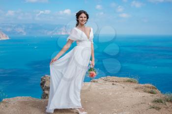 A beautiful bride standing on the coast. The bride in mountains. Wedding. Romantic beautiful bride in white dress posing on the background sea