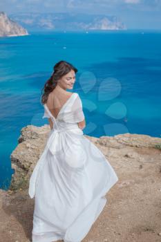 A beautiful bride standing on the coast. The bride in mountains. Wedding. Romantic beautiful bride in white dress posing on the background sea
