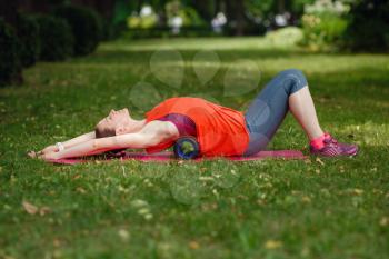 A young woman does stretching with a special roller in the park. The idea and concept of a healthy lifestyle