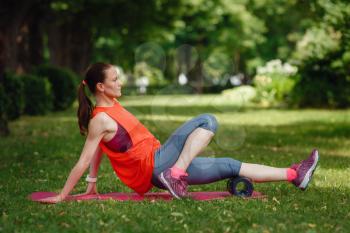 A young woman does stretching with a special roller in the park. The idea and concept of a healthy lifestyle