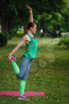 Young fitness woman runner stretching and warming up legs before run. The idea and concept of a healthy lifestyle, preparing for physical exertion. Green park summer afternoon