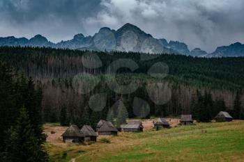path through Gasienicowa Valley in Tatry mountains, Poland. Gloomy autumn weather over beautiful wooden houses in the meadows in the foothills.