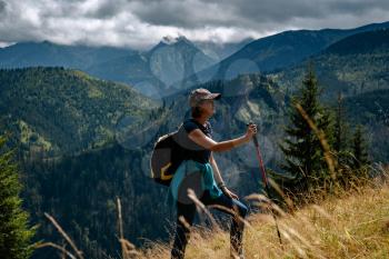 A young woman with a backpack and a tracking stick is climbing a mountain. Tatra National Park, Poland