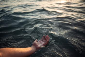 Woman hands in water inviting you over sunset golden rays. Summer vacation and travel concept
