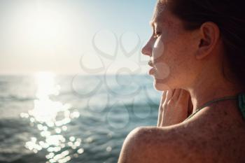 Ginger girl with freckles in a bikini looks at a beautiful sunset over the sea. Idea and concept of relaxation, freedom, vacation and happiness