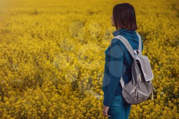 Woman traveler in a blue sweater and jeans in a flowering rapeseed field. Happy beautiful young woman enjoys smell of blooming rapeseed field full of joy and happiness. Concept of freedom
