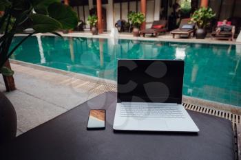 White Laptop at the swimming pool and smartphone, workspace at a freelancer on vacation.