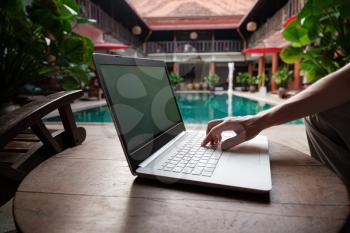 travel blogger sitting at swiming pool writing article on white laptop. Freelance remote work concept. Self employed man coding. Copy space, pool view background