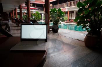 A white laptop on wooden table swiming pool background. A start of new day. Freelance business concept. Flexible remote working, travelling, advert and copy space
