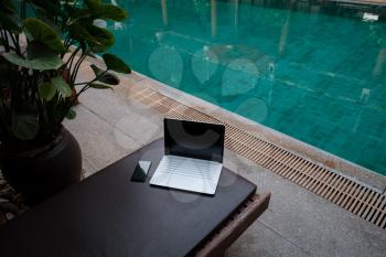 White Laptop at the swimming pool and smartphone, workspace at a freelancer on vacation.