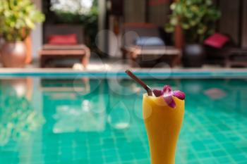 fresh tropical smoothie or mango juice in a tall glass on the background of the pool