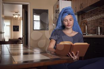 Young asian woman after bath in towel reads a book in the kitchen. Natural beauty healthy model happy enjoying self isolation. stay at home social media campaign for coronavirus prevention