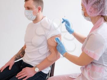 immunization procedure and approving vaccination. Female nurse in pink uniform with protective mask vaccinate millennial male Caucasian patient