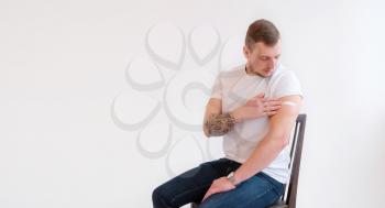 Man in white T-shirt smiling after receiving vaccination on white background. Man showing his arm after receiving a vaccine.