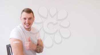 Man in white T-shirt smiling after receiving vaccination on white background. Man showing his arm after receiving a vaccine.