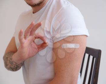 Man in white T-shirt smiling after receiving vaccination on white background. Man showing his arm after receiving a vaccine, close-up.