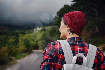 Happy young woman with backpack exploring misty mountains. Travel and wanderlust concept. Amazing atmospheric moment
