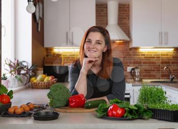 Healthy eating lifestyle concept portrait of beautiful young redhair woman preparing tasty food salat with broccoli, zucchini, red pepper, herbs on the table