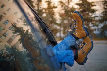 Woman feet in trendy yellow hiking boots on car door. Feet outside the window at sunset forest. The concept of freedom of movement. An autumn weekend in nature.