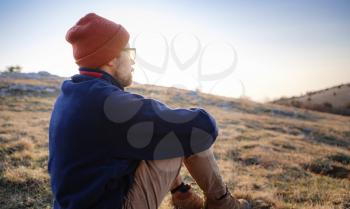 A young man sitting in spring mountains at sunset and enjoying view of nature. Mountain and coastal travel, freedom and active lifestyle