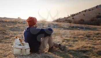 A young man sitting in spring mountains at sunset and enjoying view of nature. Mountain and coastal travel, freedom and active lifestyle