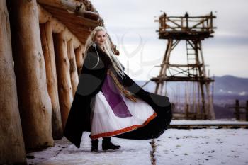 Beautiful blonde Viking dressed in a black cloak against the backdrop of the castle. beautiful film set - an ancient Viking village