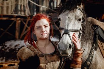 Viking girl with grey horse. Reconstruction of a medieval scene. Against the backdrop of a large viking village.