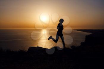 Side view of fitness woman running on a road by the sea. Sportswoman training on seaside promenade at sunset. Summer sport and freedom concept. Athlete training on dusk.