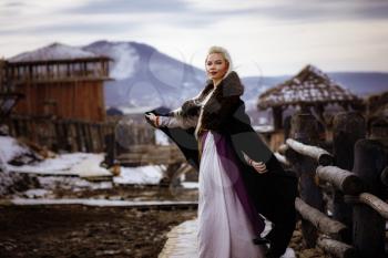 Beautiful blonde Viking dressed in a black cloak against the backdrop of the castle. beautiful film set - an ancient Viking village