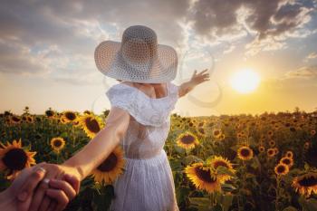 Beautiful young girl enjoying nature on the field of sunflowers at sunset. idea and concept - follow me