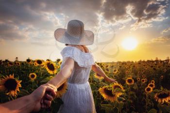 Beautiful young girl enjoying nature on the field of sunflowers at sunset. idea and concept - follow me