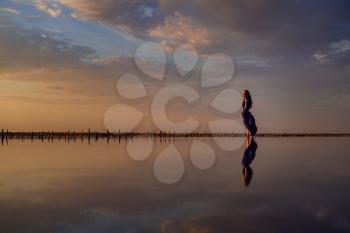 Elegant woman in silky purple dress walking by a salt lake. Romantic mood. Water reflection of clouds and empty space. Holiday, vacation travel scene. glorious sky at sunset