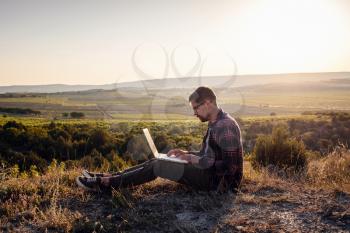 man with laptop sitting on the edge of a mountain with stunning views of the valley. Cellular network broaband coverage concept. 5G.