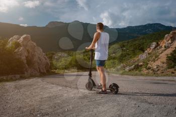 Young man riding an electric scooter on mountain range. Ecological transportation concept