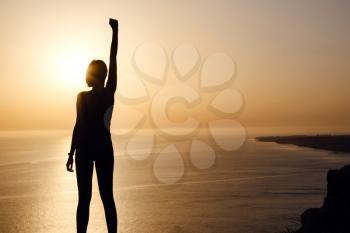 silhouette of woman with raised hands on the beach at sunset. People success, victory, and power. Strong woman, Winning, success , and life goals concept.