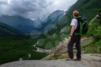 Man hiking at mountains with heavy backpack. Travel Lifestyle wanderlust adventure concept, summer vacations outdoor alone into the wild. North Caucasus, Dombai, Russia.