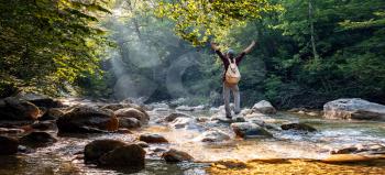 Happy male hiker raised hands outdoors in forest near river. idea and concept of adventure, discovery and travel