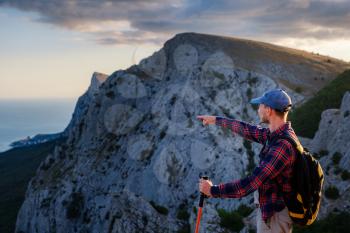 Adventurous man is on top of the mountain and enjoying the beautiful view during a vibrant sunset and points a finger. success, winner, leader concept and idea