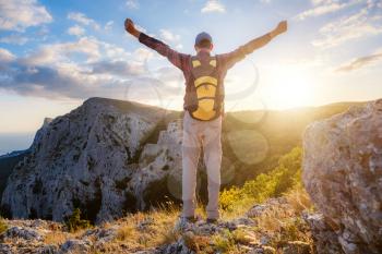 Adventurous man is on top of the mountain and with raised hands and enjoying sunrise. Successfully achieving your goal concept