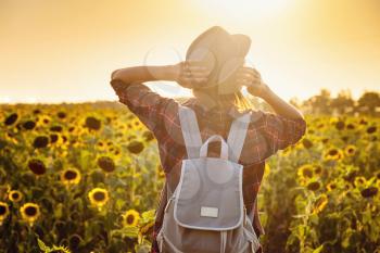 Beautiful young woman enjoying nature on the field of sunflowers. stands back and looks at the sunset,