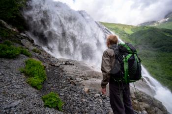 Man hiking with backpack looking at waterfall. Travel Lifestyle adventure concept, active vacations into the wild harmony with nature. North Caucasus, Dombai, Russia.
