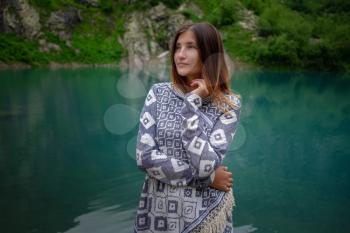 Adventure asian woman feeling freezing among mountains, enjoy the nature view. Forest and lake, wearing poncho, boho and wanderlust style. Turier lake, Alibek glacier, North Caucasus, Dombai,, Russia.