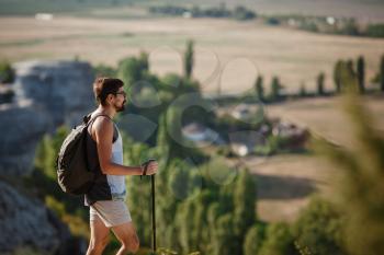 Hiking man portrait with backpack walking in nature. Caucasian man smiling happy with valley in background during summer trip.