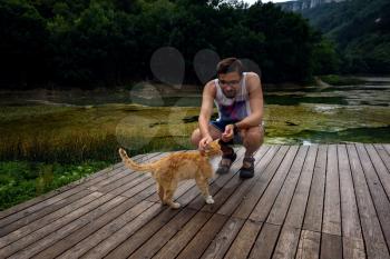 A man is playing with a domestic red tabby cat. The cat rubs on the mans leg. after the rain