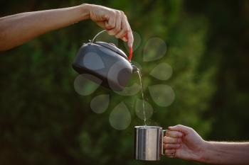 Hiker pouring a hot drink from a metal teapot into a steel mug. Atmospheric tranquil moment.